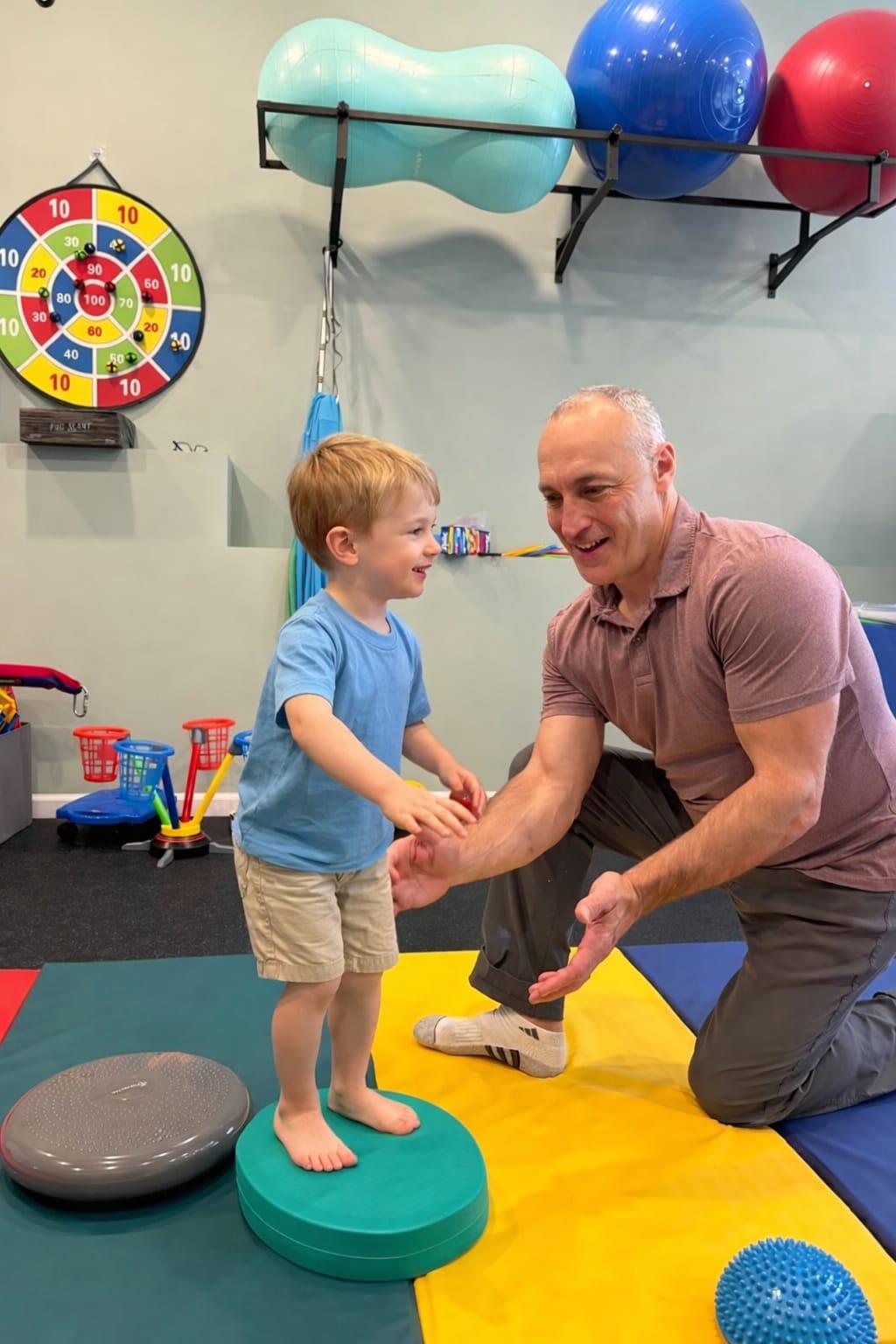 A child smiling while interacting with a therapist in a bright, modern therapy space